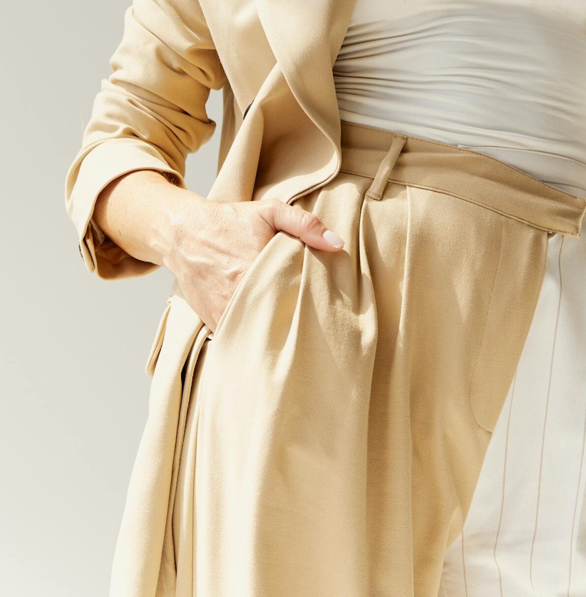 Elegant caucasian woman in a beige suit with hands in pockets, posing confidently against a neutral background.